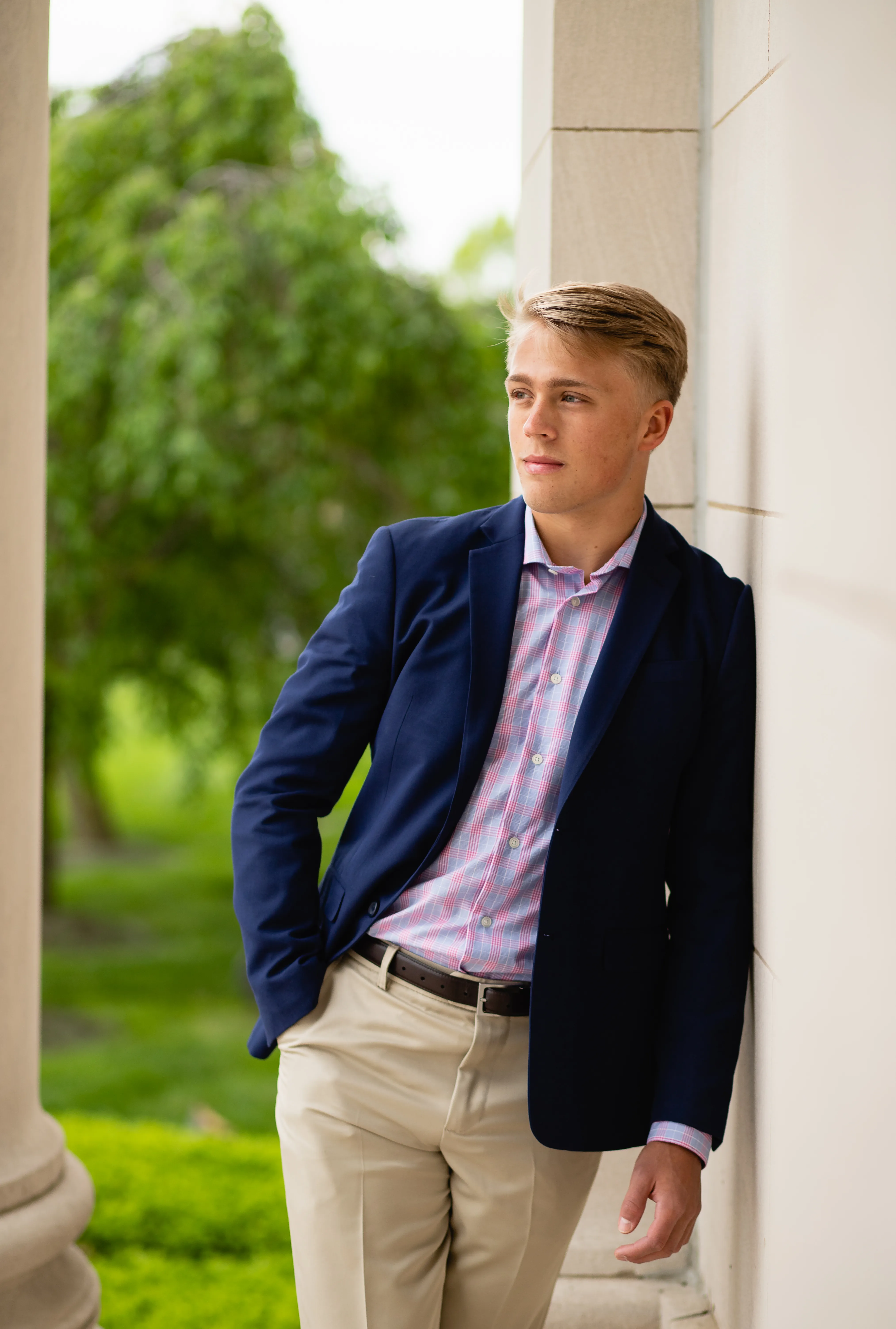 Senior in a navy blazer and khakis leaning against a stone column