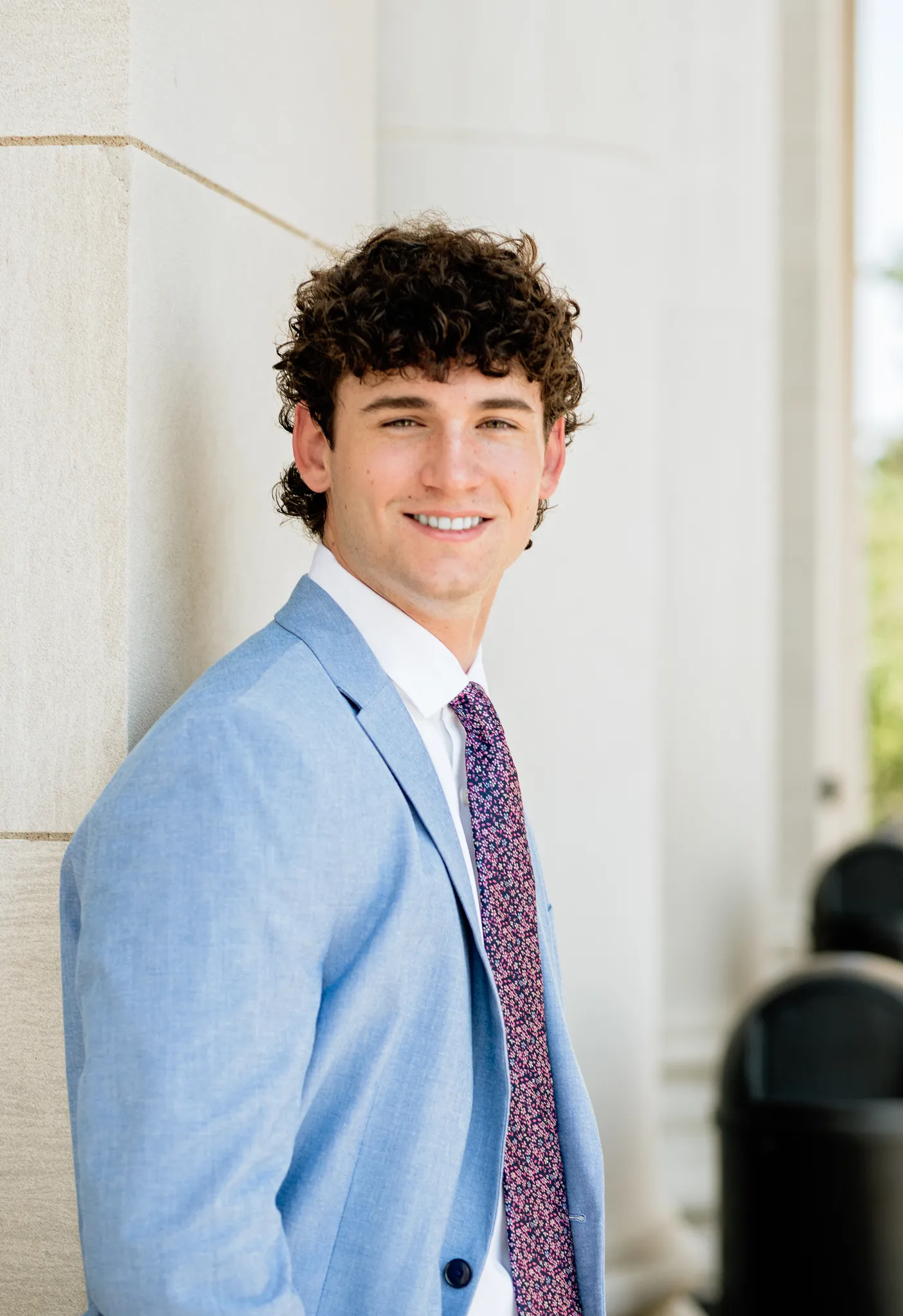 Senior in a light blue suit smiling beside limestone columns