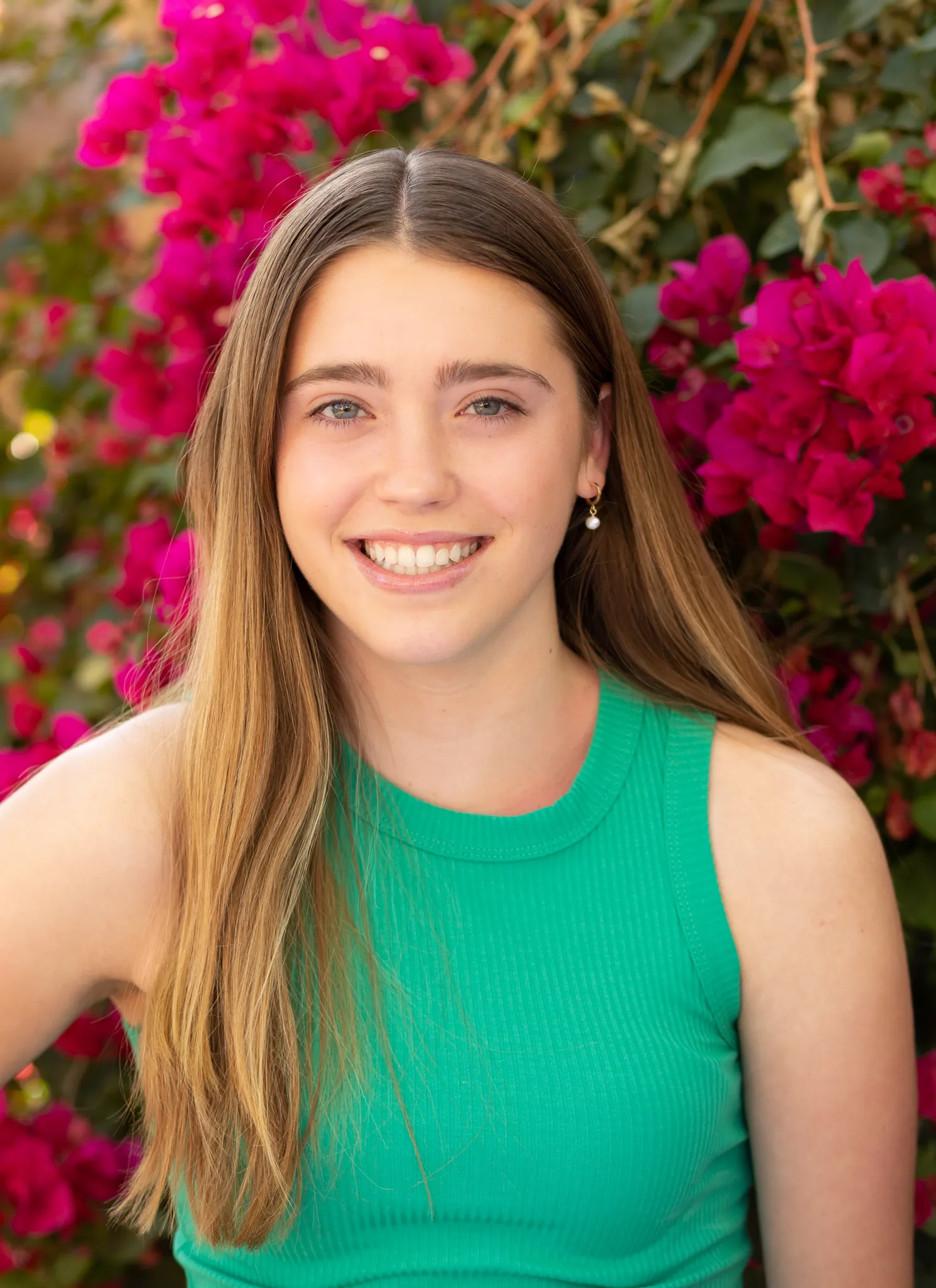 Senior in a green top smiling in front of bright pink bougainvillea