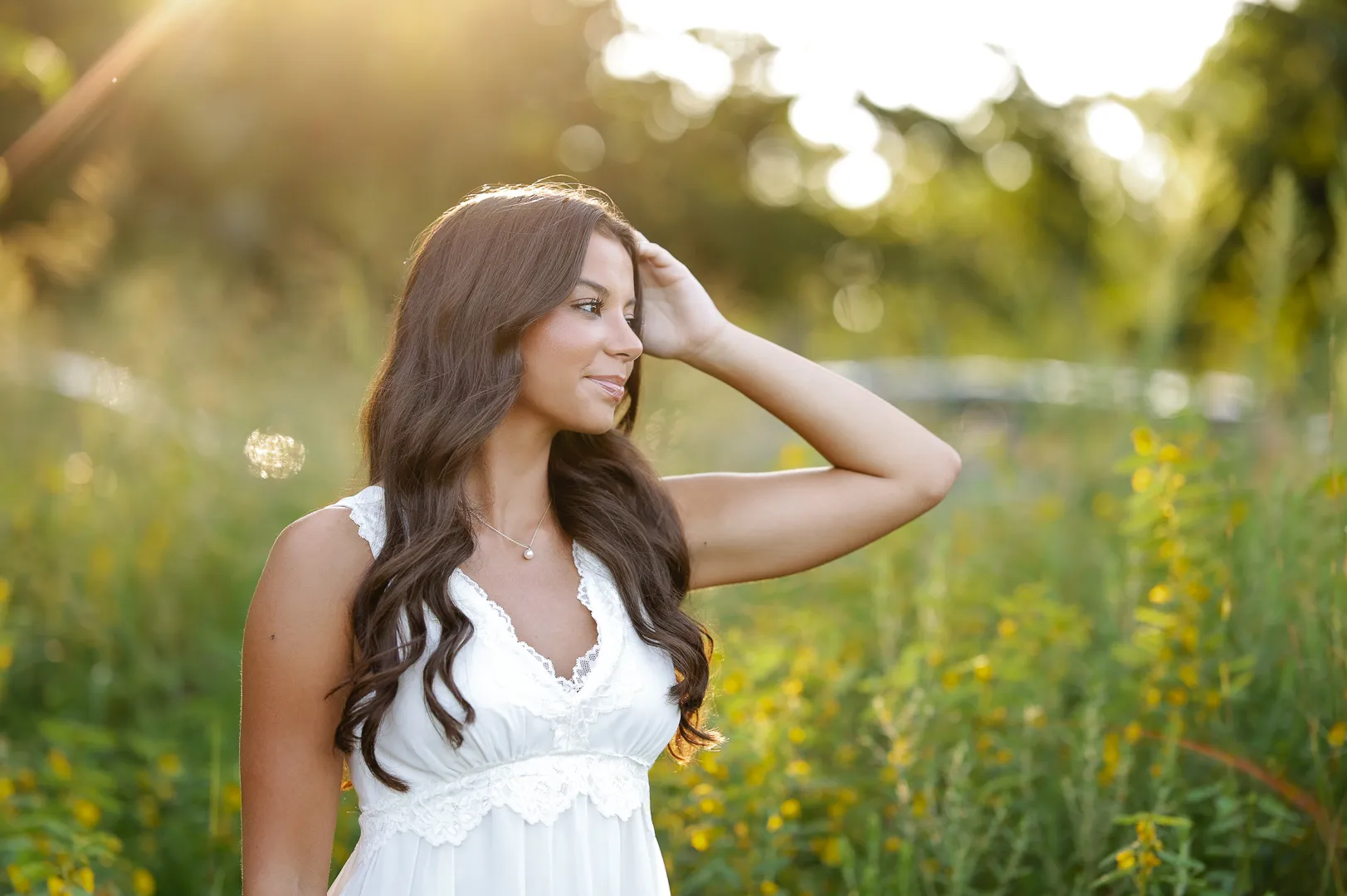 Senior in a white lace dress in a field of yellow wildflowers at golden hour