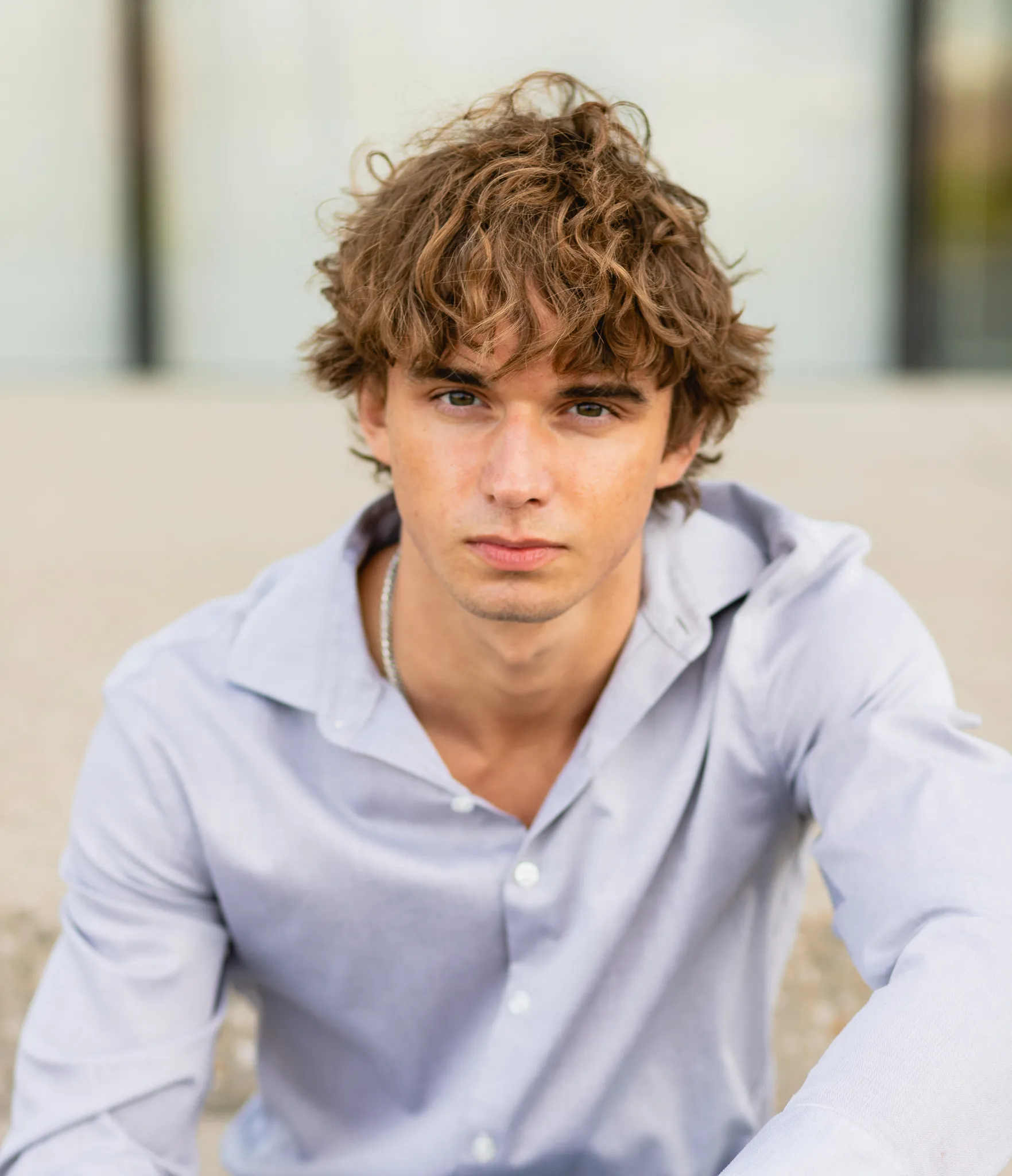 Senior with curly hair in a gray button-down, downtown light behind him