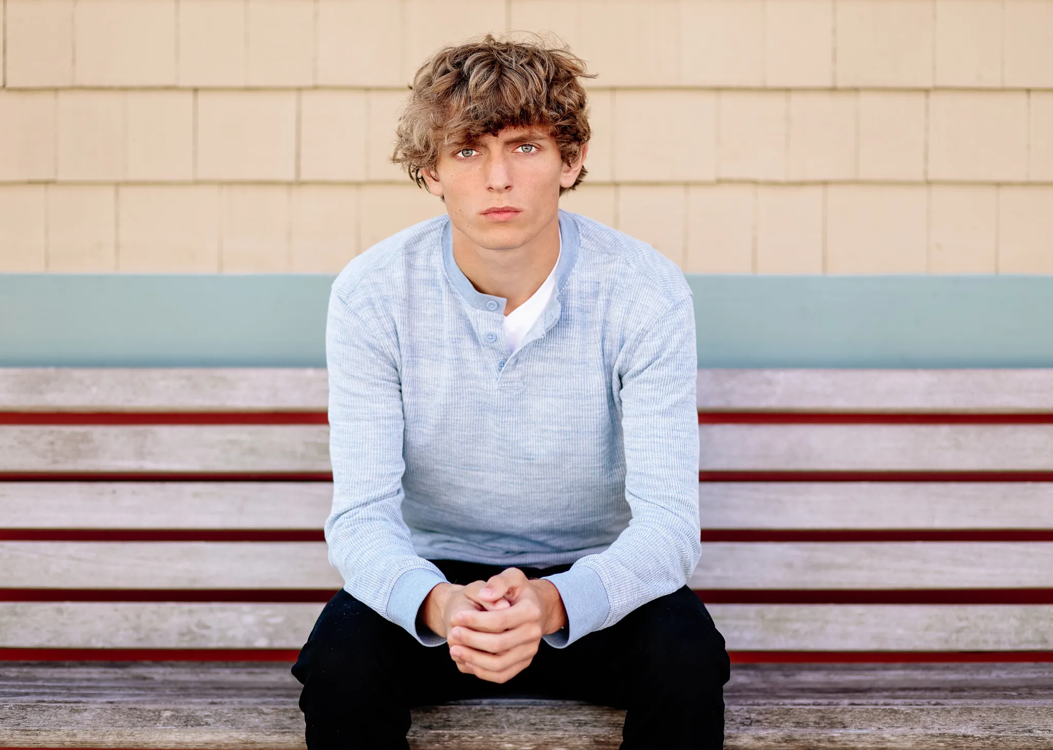 Senior in a light blue henley seated on a striped boardwalk bench