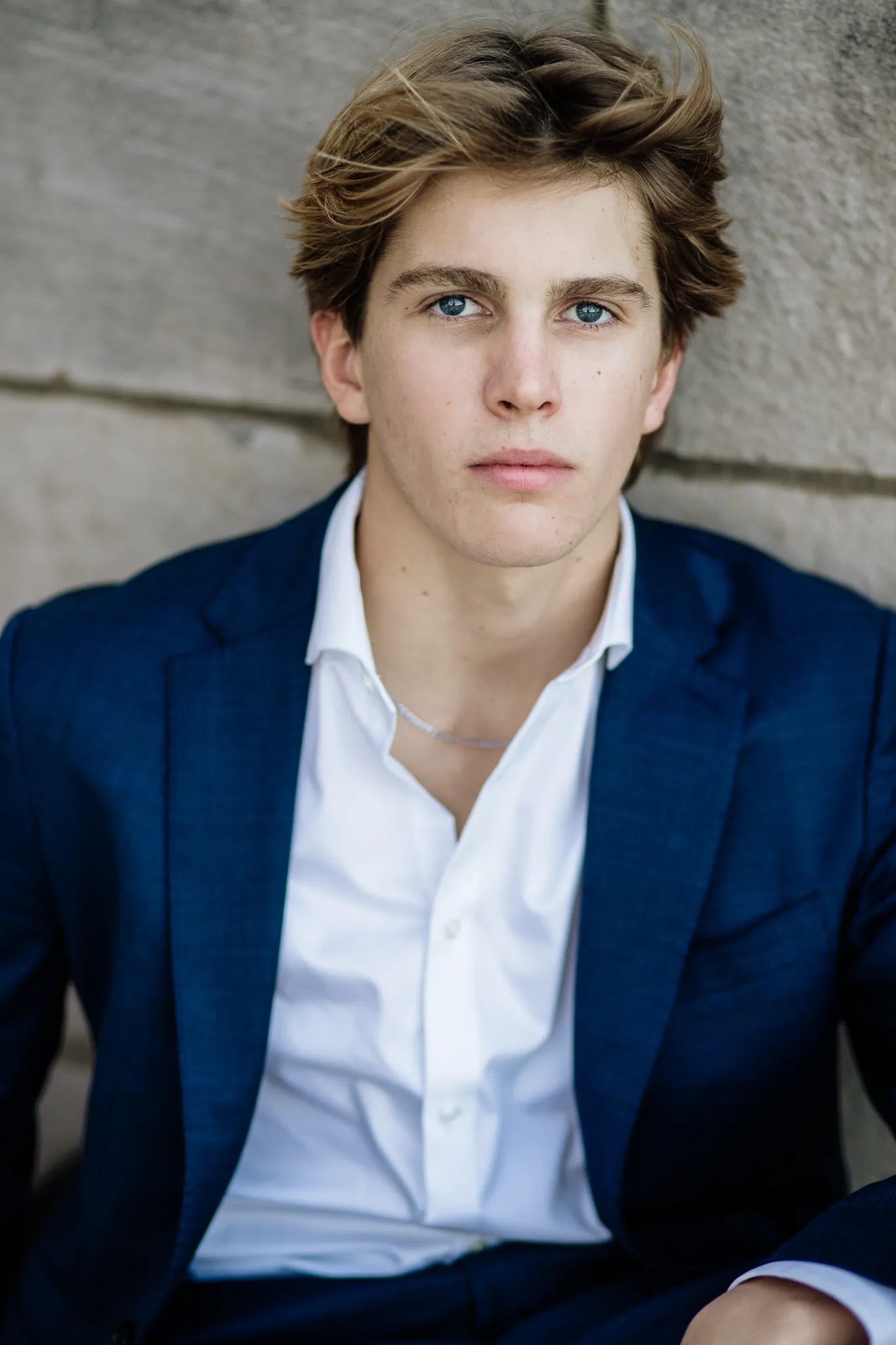 Senior in a navy blazer and open white shirt against a stone wall