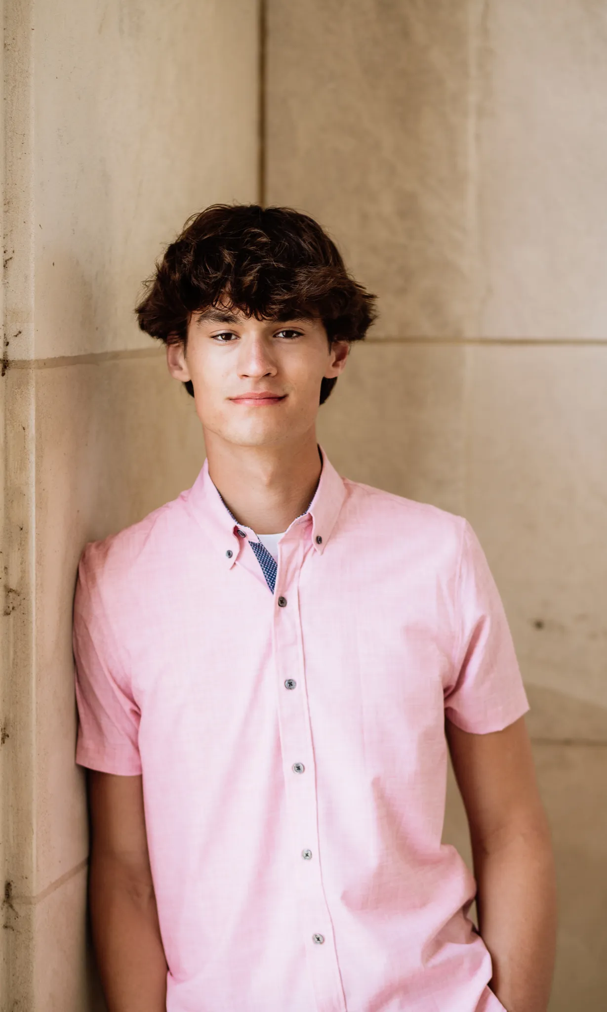 Senior in a pink button-down against a limestone wall