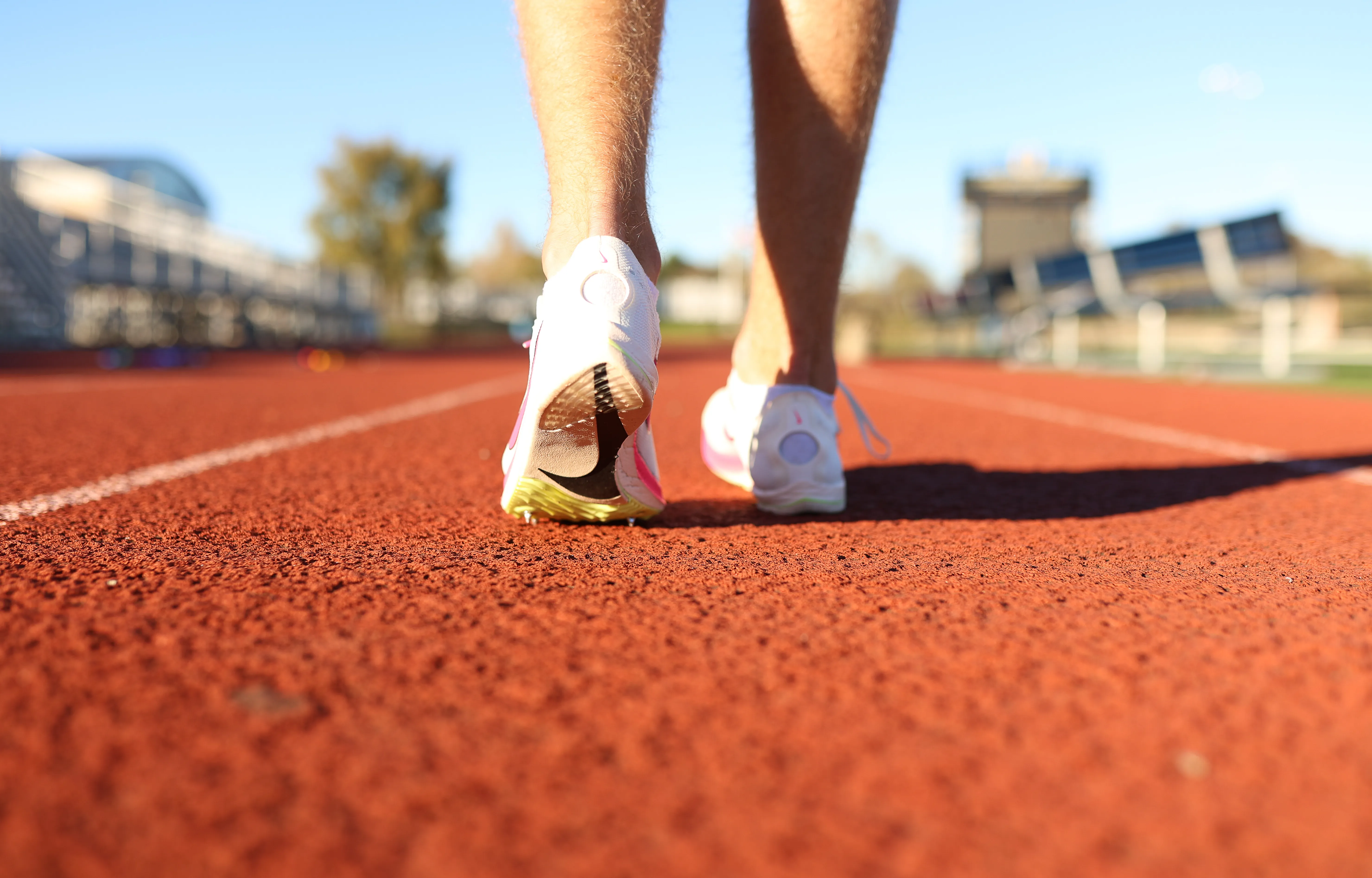 Track spikes mid-stride on the red track, seen from behind